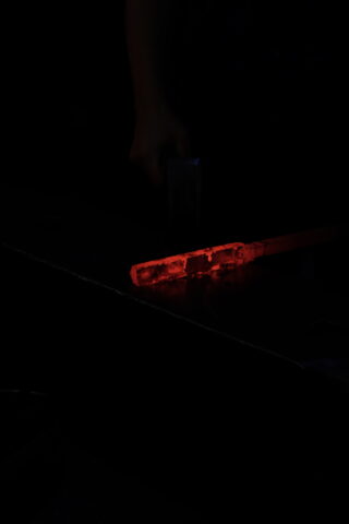 Ein glühend heißer Metallbarren wird auf einem Amboss mit einem Hammer geformt, wodurch der Schmiedeprozess bei schwachem Licht hervorgehoben wird.