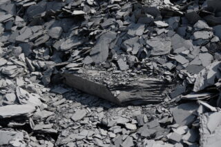 Ein Haufen grauer Schiefersteine und Scherben, mit einem großen, flacheren Stück Schiefer in der Nähe der Mitte.