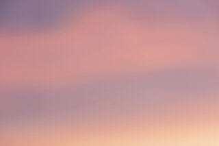 Sanft pastellfarbener Himmel mit Farbverläufen in Rosa, Lila und Orange, der einen Sonnenaufgang oder Sonnenuntergang suggeriert. Keine erkennbaren Objekte oder Merkmale.
