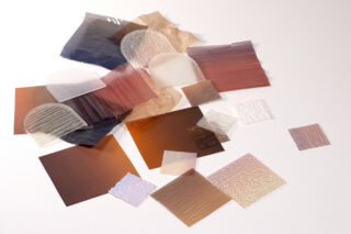 Eine Sammlung durchscheinender und undurchsichtiger, kunststoffähnlicher Filmproben in verschiedenen Größen, Formen und neutralen Farbtönen, angeordnet auf einer weißen Oberfläche.