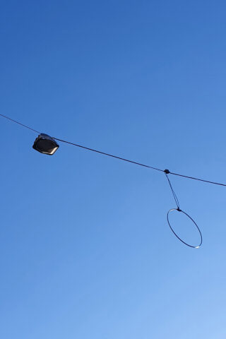 Ein Flutlicht und eine kreisförmige Kabelschleife sind an einem Draht befestigt, der vor einem klaren blauen Himmel schwebt.