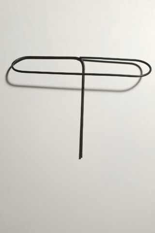 Eine große Büroklammer aus Metall ist in eine Form gebogen, die einem Großbuchstaben „T“ auf einem schlichten weißen Hintergrund ähnelt.