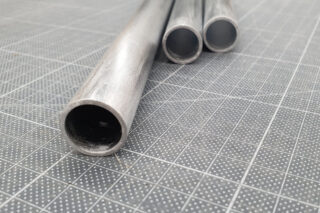 Drei Metallrohre sind auf einer gitterförmigen Oberfläche platziert, wobei sich ein Rohr im Vordergrund und zwei im Hintergrund befinden.