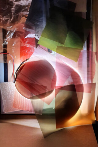 Eine Mischung aus durchscheinenden farbigen Blättern und Kunststoffauflagen, die durch Licht beleuchtet werden und so auf einer flachen Oberfläche geschichtete Reflexionen und weiche Schatten erzeugen.