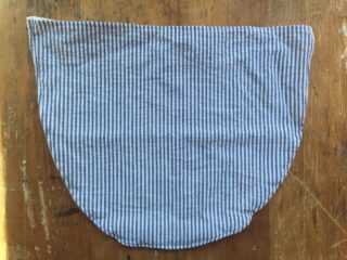 Ein blau-weiß vertikal gestreiftes Stoffstück, ungefähr oval mit flacher Oberseite, auf einer Holzoberfläche platziert.