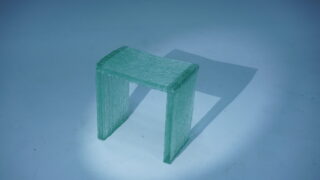 Auf einem hellblauen Hintergrund steht ein durchscheinender, rechteckiger Hocker mit strukturierter Oberfläche und wirft einen Schatten nach rechts.