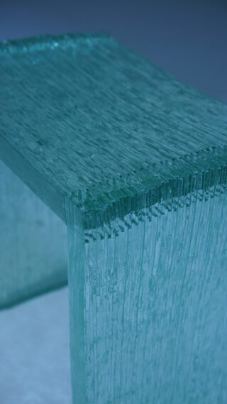 Eine Nahaufnahme einer Bank oder eines Tisches aus gestapelten, geschichteten Glasplatten mit einem durchscheinenden blaugrünen Farbton.