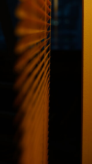 Eine Nahaufnahme von Jalousien von der Seite betrachtet, mit warmem gelbem Licht auf der rechten Seite und einem dunklen, unscharfen Hintergrund.