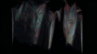 Eine zerknitterte, reflektierende Metalloberfläche mit bunten Lichtreflexen vor dunklem Hintergrund.