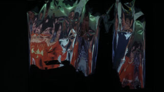 Faltige metallische oder reflektierende Oberfläche mit verzerrten Reflexionen in Grün-, Rot- und Blautönen vor schwarzem Hintergrund.