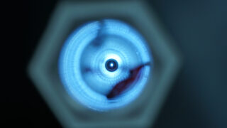 Eine Nahaufnahme, ein unscharfes Bild eines kreisförmigen blauen Lichtmusters mit konzentrischen Ringen, betrachtet durch einen sechseckigen Rahmen.