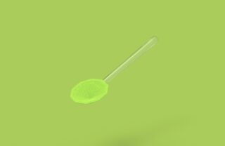 Vor einem einfarbig grünen Hintergrund hängt ein transparenter Löffel, der mit grünem Pulver gefüllt ist.