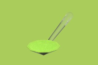 Ein durchsichtiger Plastiklöffel mit einem kleinen Haufen grünem Pulver vor einem hellgrünen Hintergrund.