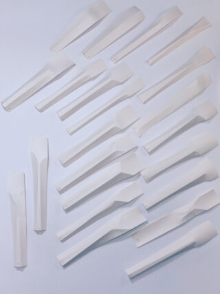 Achtzehn identische weiße Papierobjekte mit gefalteten Formen sind in Reihen auf einer flachen weißen Oberfläche angeordnet.