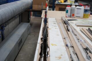 Eine Werkbank mit verschiedenen Werkzeugen, Materialien und Flaschen, darunter eine lange Form, die mit dunklem flüssigem Harz oder Klebstoff gefüllt ist, in einer Werkstattumgebung.