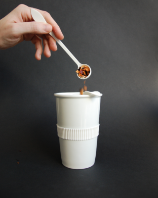 Eine Hand lässt Teeblätter in eine Porzellantasse fallen.