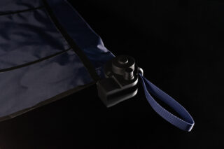 Eine Nahaufnahme einer Ecke eines dunklen Stofftuchs mit einem schwarzen Kunststoffaufsatz und einem blauen gewebten Riemen vor einem schwarzen Hintergrund.