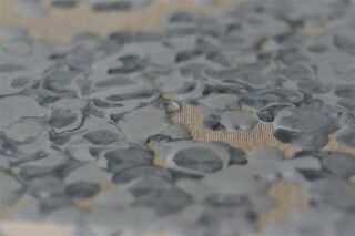 Nahaufnahme einer strukturierten Oberfläche mit unregelmäßigen, erhabenen grauen Formen auf beigem Hintergrund.