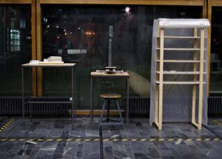 Drei Arbeitsplätze mit Hocker, kunststoffverkleidetem Regal, Geräten auf Tischen und einem großen Fenster im Hintergrund.