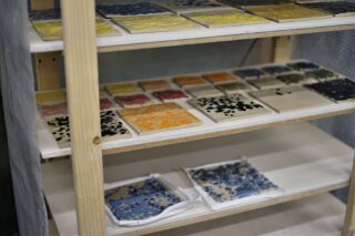 Regale mit mehreren Fliesen mit unterschiedlichen farbigen Glasuren und Mustern, die wahrscheinlich in einem Studio oder einer Werkstatt trocknen oder gelagert werden.