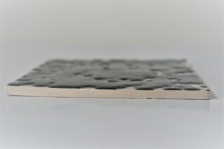 Eine von der Seite fotografierte Keramikfliese mit einer strukturierten, glänzenden dunklen Oberfläche auf der Oberseite und einer glatten, unglasierten Kante und Unterseite.