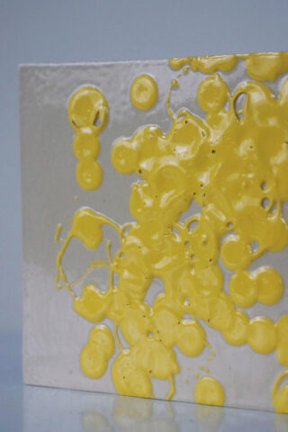 Eine rechteckige metallische Oberfläche mit Ansammlungen glänzender, erhabener gelber Punkte, die unregelmäßig über einen Teil der Oberfläche verteilt sind.