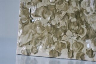 Nahaufnahme einer strukturierten, glänzenden Oberfläche mit einem unregelmäßigen, organischen Muster in Beige- und Hellbrauntönen auf reflektierendem Hintergrund.