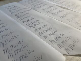 Mehrere weiße Blätter Papier, auf denen auf jeder Seite wiederholt mit schwarzer Tinte der Name „M. Marlo“ handschriftlich steht.