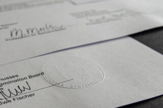 Nahaufnahme offizieller Dokumente mit handschriftlichen Unterschriften und geprägtem Notarsiegel.