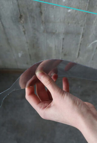 Eine Hand hält ein dünnes, flexibles, transparentes Blatt vor dem Hintergrund einer rauen Betonwand.