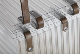Nahaufnahme von klaren, gerippten Glas- oder Kunststoffplatten, die durch braune Metallklammern mit Schrauben zusammengehalten werden.