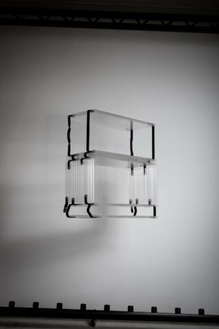 Zwei übereinander gestapelte, transparente rechteckige Boxen sind mit schwarzen Klammern vor einem schlichten Hintergrund an einer Wand befestigt.