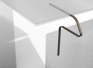 Eine rechtwinklig gebogene Metallstange wird über die Kante einer durchscheinenden Wellplatte gehakt, wobei Licht und Schatten auf den darunter liegenden weißen Flächen sichtbar werden.