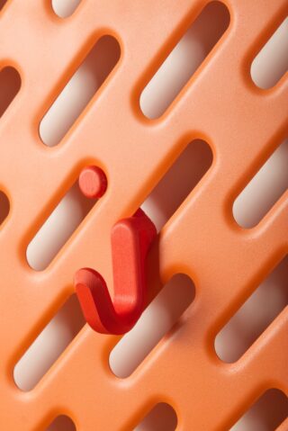 Nahaufnahme einer orangefarbenen Lochplatte mit länglichen ovalen Löchern, in die ein einzelner roter Haken und ein kleiner roter runder Stift eingesetzt sind.