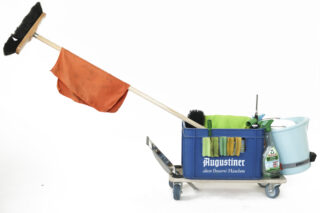 Ein Reinigungswagen mit Besen, orangefarbenem Tuch, blauem Eimer, Reinigungsmitteln und Bürsten auf einem Metallrahmen mit Rädern vor weißem Hintergrund.