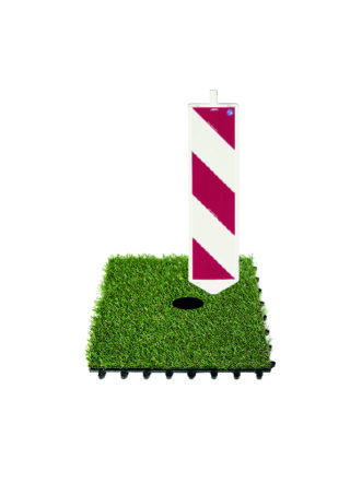 Ein quadratischer Kunstrasenfleck mit schwarzer Basis und einem vertikalen weißen Schild mit diagonalen roten Streifen in der Nähe einer Ecke.