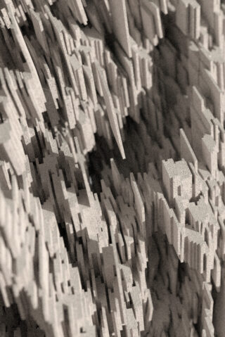 Eine Nahaufnahme einer abstrakten, dreidimensionalen Struktur aus zahlreichen beigefarbenen rechteckigen Blöcken, die ungleichmäßig angeordnet sind und so eine raue, gezackte Oberfläche bilden.