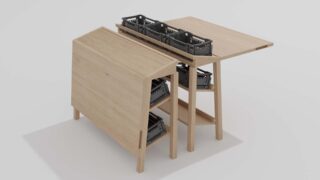 Ein Holztisch mit zwei Höhen hält vor einem schlichten Hintergrund drei schwarze Plastikkörbe auf der oberen Ebene und zwei auf der unteren Ablage.