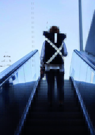 Eine Person mit lockigem Haar und einem großen schwarzen Rucksack mit weißen X-Trägern steht mit dem Gesicht nach oben auf einer Rolltreppe in einer Innenumgebung mit blau getöntem Hintergrund.