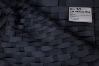 Dunkler Webstoff mit dem Etikett „No. 3/3 THE VIRTUAL FOLD 2021“ sowie Pflegesymbolen und Text mit Hinweisen zur chemischen Reinigung und Materialdetails.
