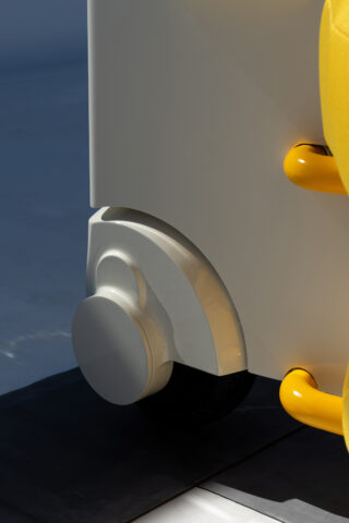 Nahaufnahme eines modernen weißen Lenkrads, das an einem Möbelstück mit glatter Oberfläche und gelben Griffen befestigt ist.