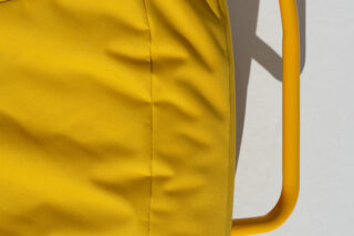 Nahaufnahme eines gelben Stoffkissens auf einem gelben Metallstuhl vor einem hellen Hintergrund.