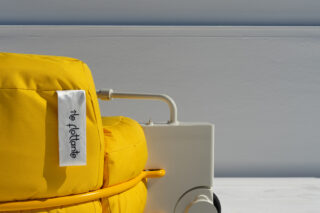 Nahaufnahme eines gelb gepolsterten Stuhls mit der Aufschrift „île flottante“, neben einem weißen Metallrahmen und Rad vor einem hellgrauen Hintergrund.