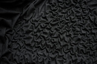 Nahaufnahme eines schwarzen Stoffes mit einer gerafften, gerüschten Textur, die unregelmäßige, sich kreuzende Falten und Grate bildet.