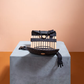 Ein Rucksack aus Holzlatten, schwarzen Riemen und Filz steht auf einem grauen Sockel vor einem pfirsich- und orangefarbenen Hintergrund.