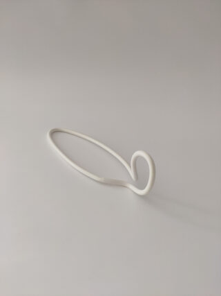 Eine weiße, minimalistische, abstrakte Keramikskulptur mit einer Schleifenkurve an einem Ende vor einem schlichten hellen Hintergrund.