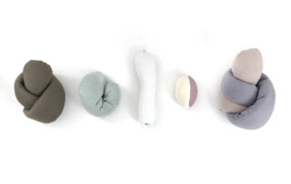 Fünf weiche Stoffobjekte unterschiedlicher Form und gedeckter Farbe sind in einer Reihe auf weißem Hintergrund angeordnet.