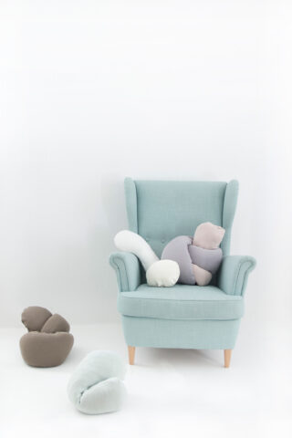 Ein hellblauer Sessel mit weichen, wolkenförmigen Kissen in neutralen Farben darauf und darum herum, vor einem schlichten weißen Hintergrund.