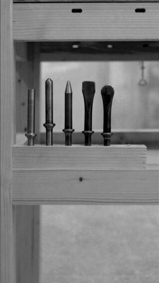 Vier Holzbearbeitungswerkzeuge aus Metall stehen aufrecht in einem Holzhalter, der an einer Werkbank befestigt ist.