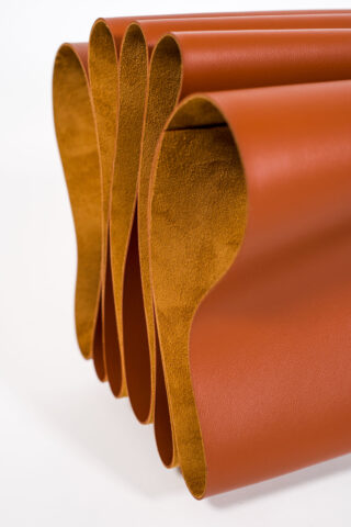 Mehrere große Blätter aus braunem Leder sind in einer ziehharmonikaartigen Anordnung hin und her gefaltet, sodass sowohl die glatte als auch die Wildlederseite sichtbar sind.